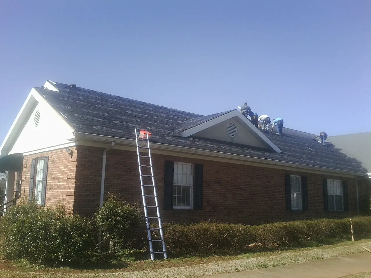 Crew tearing shingles off a brick ranch roof with a ladder set — Emergency Roof Repair work by our crew in Fenton
