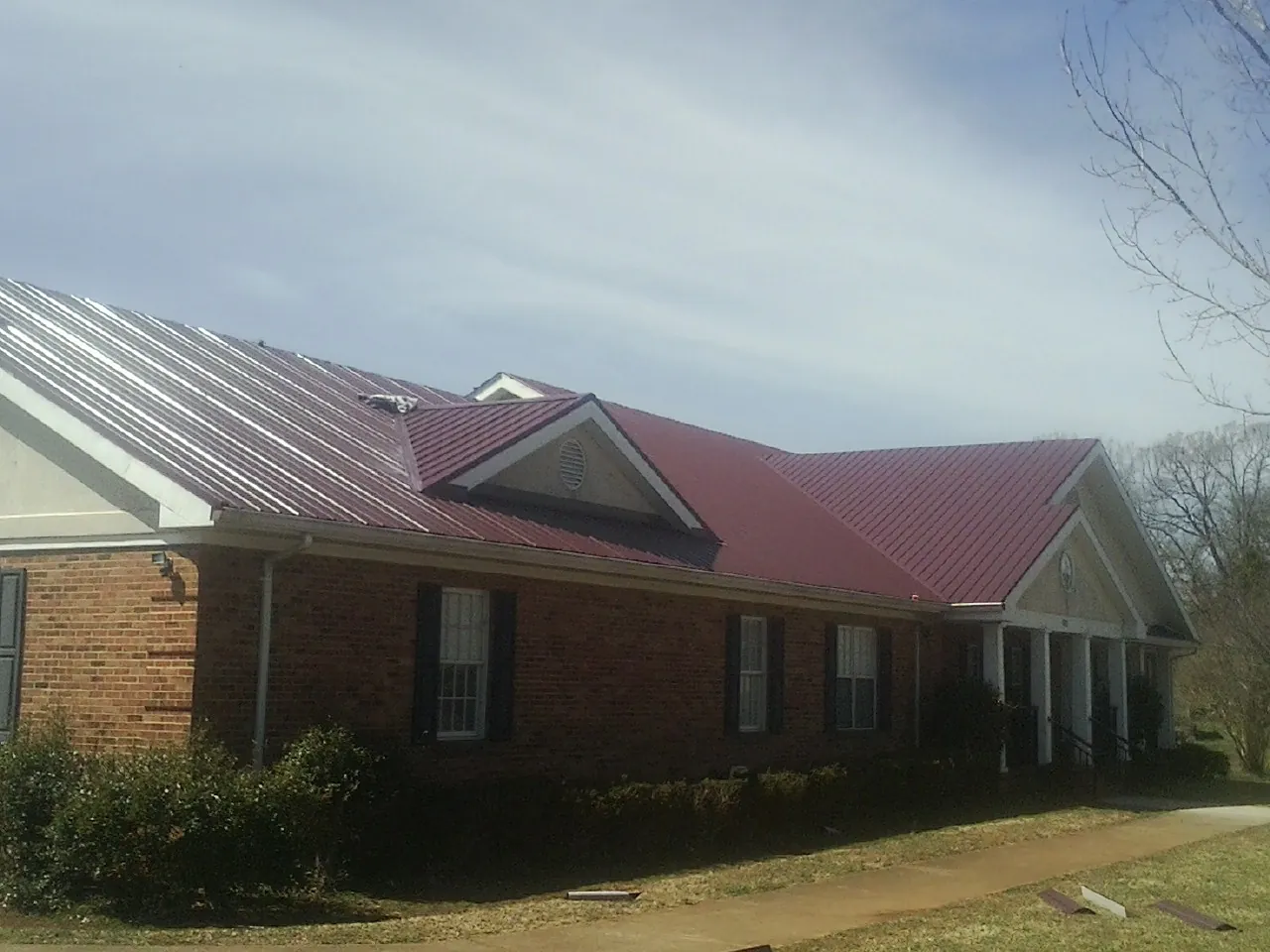 Red metal roof with gabled entries on a long brick building, from a Hail Damage Roof Repair job in Fenton